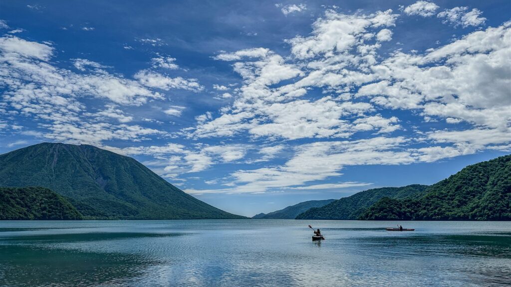 夏の中禅寺湖をカヤックで漕ぐ参加者。背景に男体山と青空