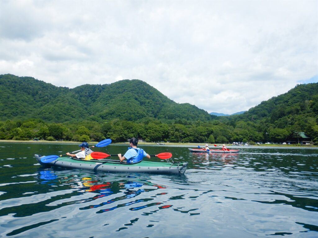 中禅寺湖を複数のカヤックで進む日中のツアー。奥日光の山々を背に